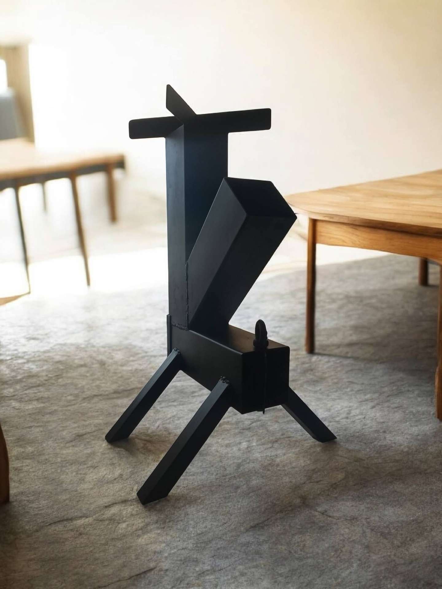 Black steel rocket stove with angular geometric body and tripod legs
